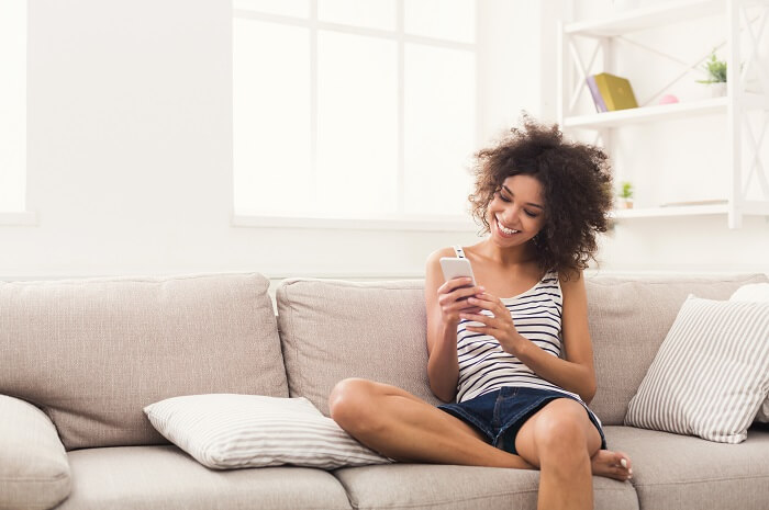 Mulher negra sentada em sofá mexendo em smartphone