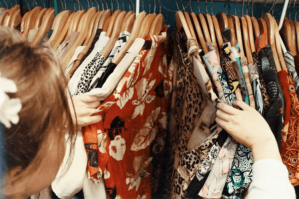 Aproveite a Black Friday para conquistar novos clientes Mulher olhando roupas penduradas em cabides