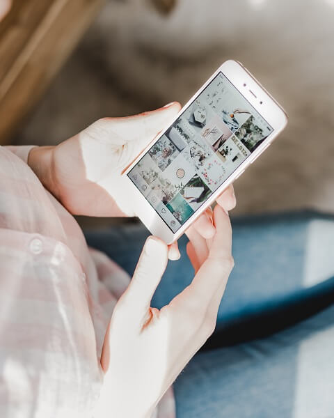 Ter os produtos da sua loja no Instagram ajudará a aumentar as vendas no Natal Mulher segurando um celular aberto em uma página do Instagram