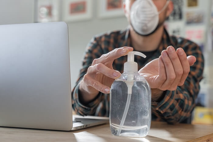 Homem branco higienizando mãos com álcool em gel