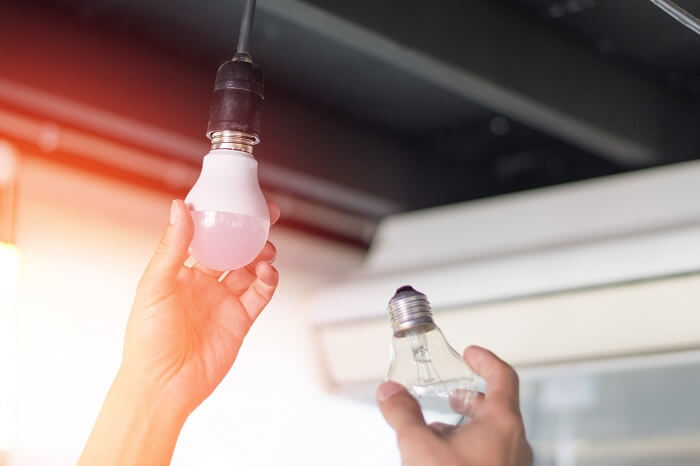 Mãos substituindo lâmpada antiga por lâmpada LED