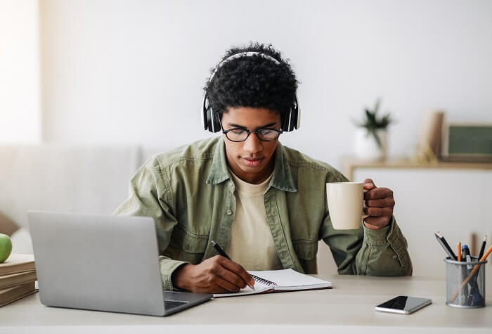 Homem negro escutando com headphones enquanto faz anotações